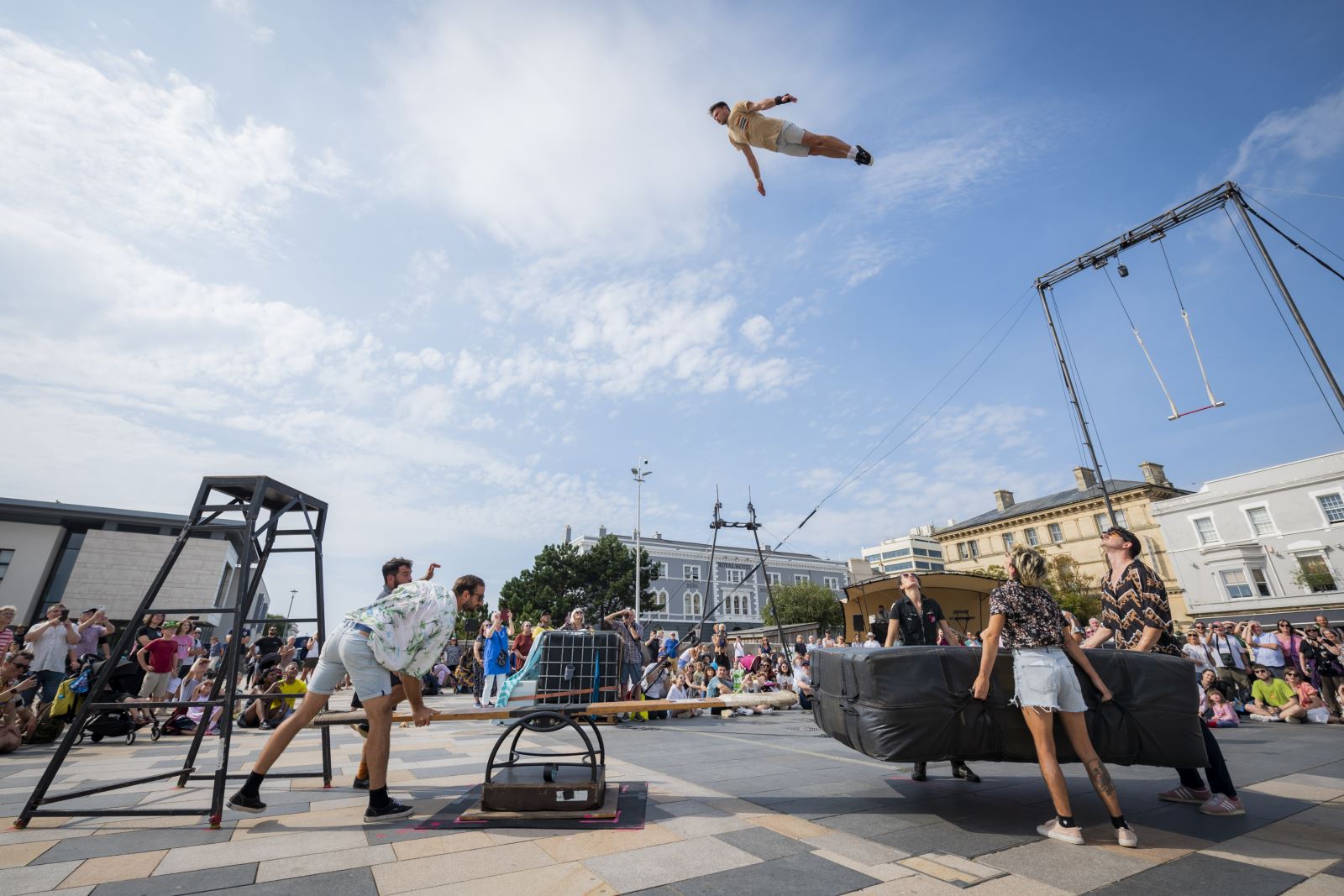 An acrobat high in the sky above some apparatus and a crowd of spectators